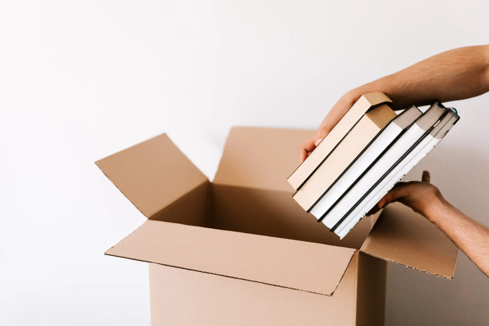 Hands placing a stack of hardback books into a cardboard box